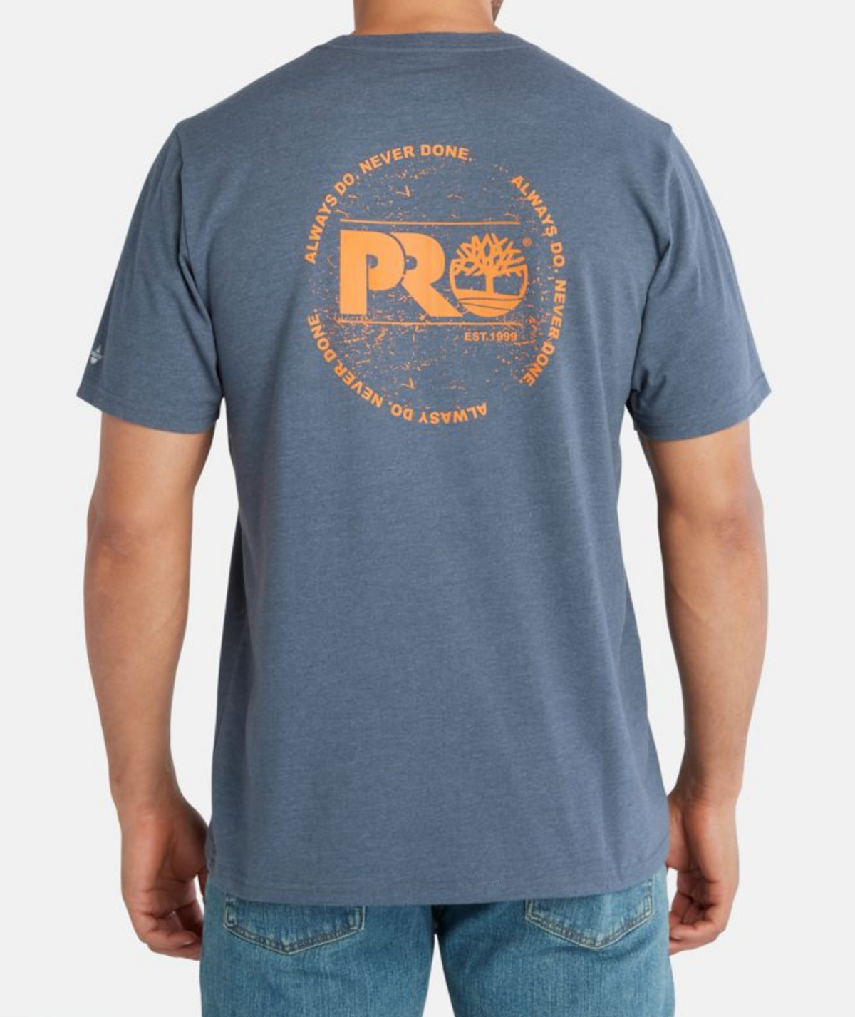 Wearing the Timberland Pro Base Plate A.D.N.D Graphic Tee, a moisture-wicking blue T-shirt with an orange circular back design featuring "PRO" and "Always Do. Never Done." above faded graphics, paired with blue jeans for seamless style and performance.