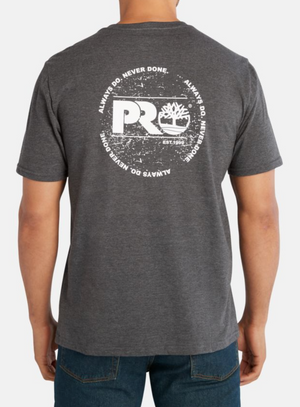 Man in a Timberland Pro Base Plate A.D.N.D Graphic Tee made from recycled polyester, showcasing a gray T-shirt with a large circular white graphic on the back, including "PRO," tree logo, "Est. 1992," and "ALWAYS DO. NEVER DONE." Paired with dark blue jeans for moisture-wicking comfort.
