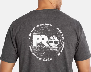 A person wearing the Timberland Pro Base Plate A.D.N.D Graphic Tee is seen from the back, showcasing a gray tee with a white circular design featuring "PR" and a tree logo. Encircled by "ALWAYS DO. NEVER DONE. EST. 1999," it's crafted from moisture-wicking, recycled polyester for comfort and sustainability.