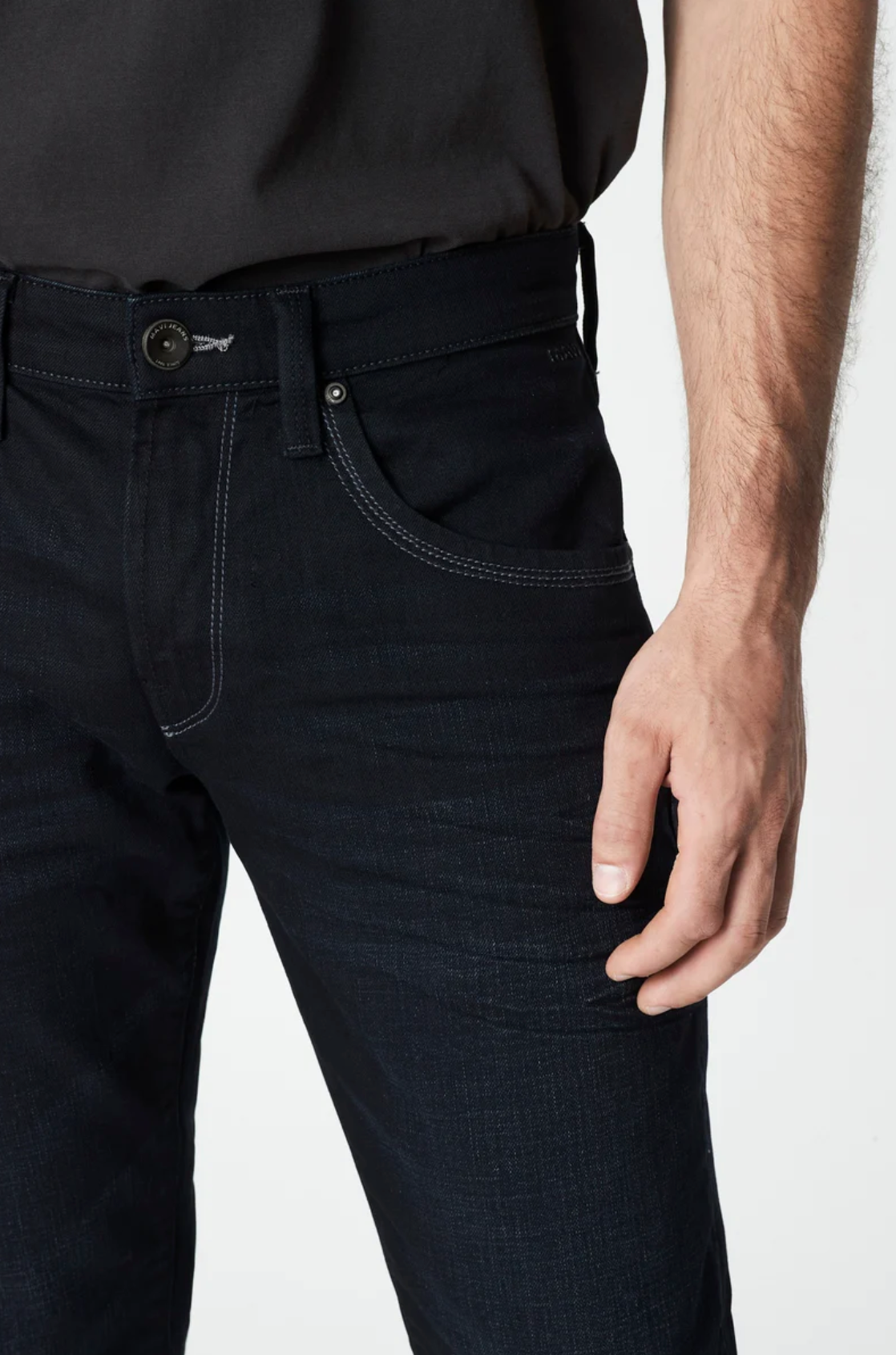 A person is pictured in the Mavi Marcus Slim Straight Jeans and a dark shirt, with their right hand near the pocket. The jeans feature a visible button and contrasting stitching, exuding a casual vibe against the plain white background.