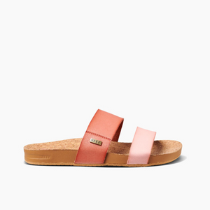 The REEF Cushion Vista Duo sandal features two coral pink straps over a cork footbed, with a cushion bounce midsole for ultimate comfort. Its flat rubber sole and small metallic brand logo on one strap complete the look, all presented against a plain white background.
