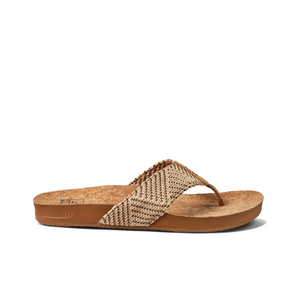 The REEF Cushion Strand is a brown flip-flop sandal with woven fabric straps in a zigzag pattern. Featuring a cork-style footbed, it offers arch support and a cushion bounce midsole for comfort, combining style and ease with its flat sole and casual design.