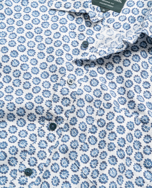 Close-up of the Rodd & Gunn First Avenue Shirt, showcasing a blue and white floral pattern. This 100% cotton button-up features intricate blue flowers on a white background, visible buttons down the center, and a stylish spread collar.