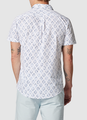 A person in a 100% cotton Rodd & Gunn Penguin Place Sports Fit Shirt with a blue diamond pattern and light blue pants, seen from the back. The shirt highlights intricate tattoos on both arms.