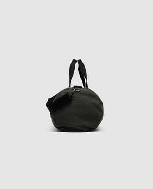 The Rodd & Gunn Double Barrel Duffle Bag is cylindrical, black, and crafted from durable cotton canvas. It features attached straps and a small side pouch, photographed upright on a plain gray background to emphasize its shape and texture.