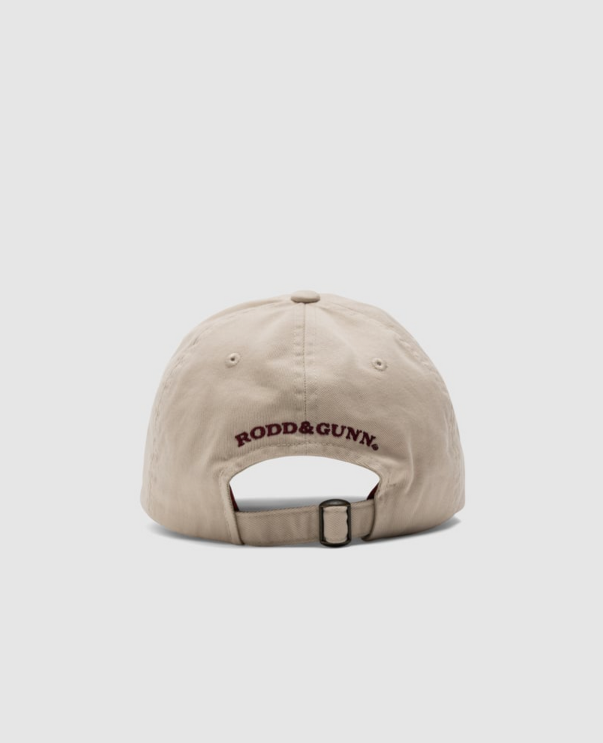 The beige Rodd & Gunn Gunn Cap, made of heavy-duty cotton twill, features the "RODD & GUNN" logo in dark red above its adjustable strap. The plain white background accentuates the cap's elegance when viewed from the back.