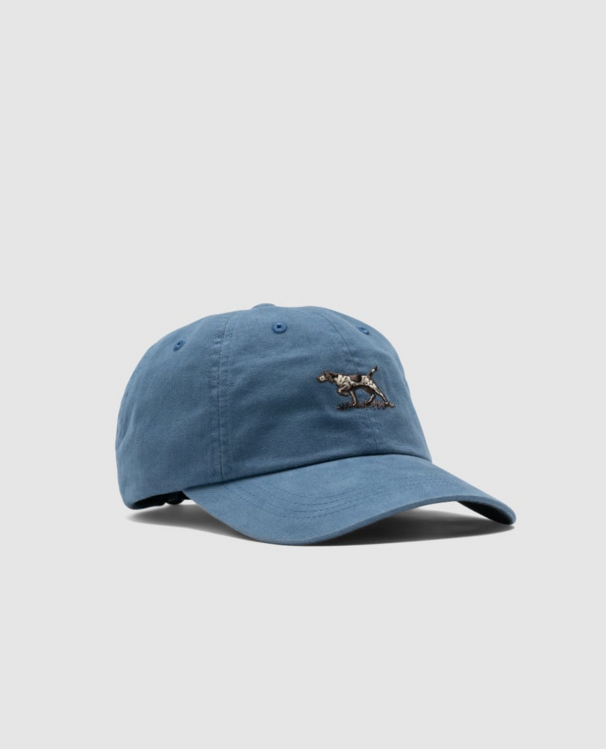 The Rodd & Gunn Signature Cap is a blue cotton twill baseball cap with a small embroidered horse and rider on the front. It features a curved brim, an adjustable back strap, and a plain gray background.