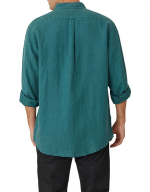 The person is wearing the Industrie The Tennyson Linen Shirt, a relaxed fit teal long-sleeve 100% linen shirt with rolled-up sleeves, paired with black pants against a plain white backdrop.