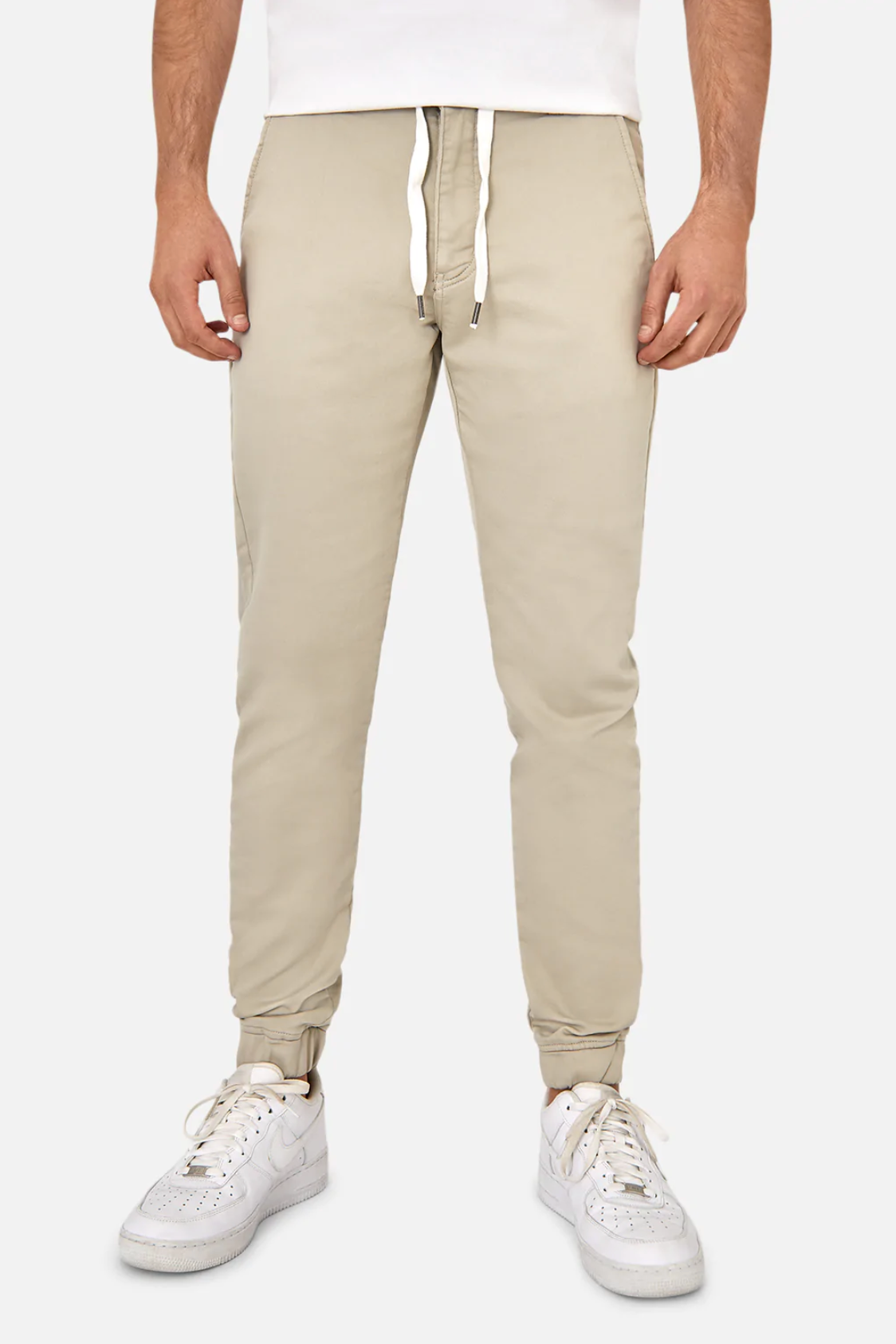A person wearing beige Industrie The Drifter Chino Pants with an elastic waist and white sneakers stands against a plain background. The chinos have a slim fit, tapered design with elastic cuffs at the ankles.