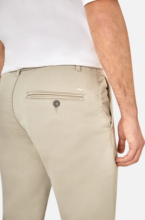 A person wearing Industrie The Drifter Chino Pant, slim fit light beige chinos with an elastic waist and a button-secured back pocket, paired with a white shirt. The photo highlights the fabric and design details from the back and pocket area.