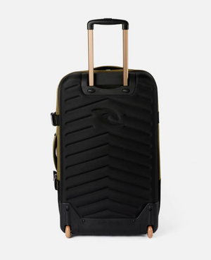 The Rip Curl F-Light Global 110L Overland Travel Bag is a spacious black hard-shell suitcase made from recycled polyester with subtle diagonal grooves, a tan telescopic handle, and two rolling wheels, all against a plain white background.