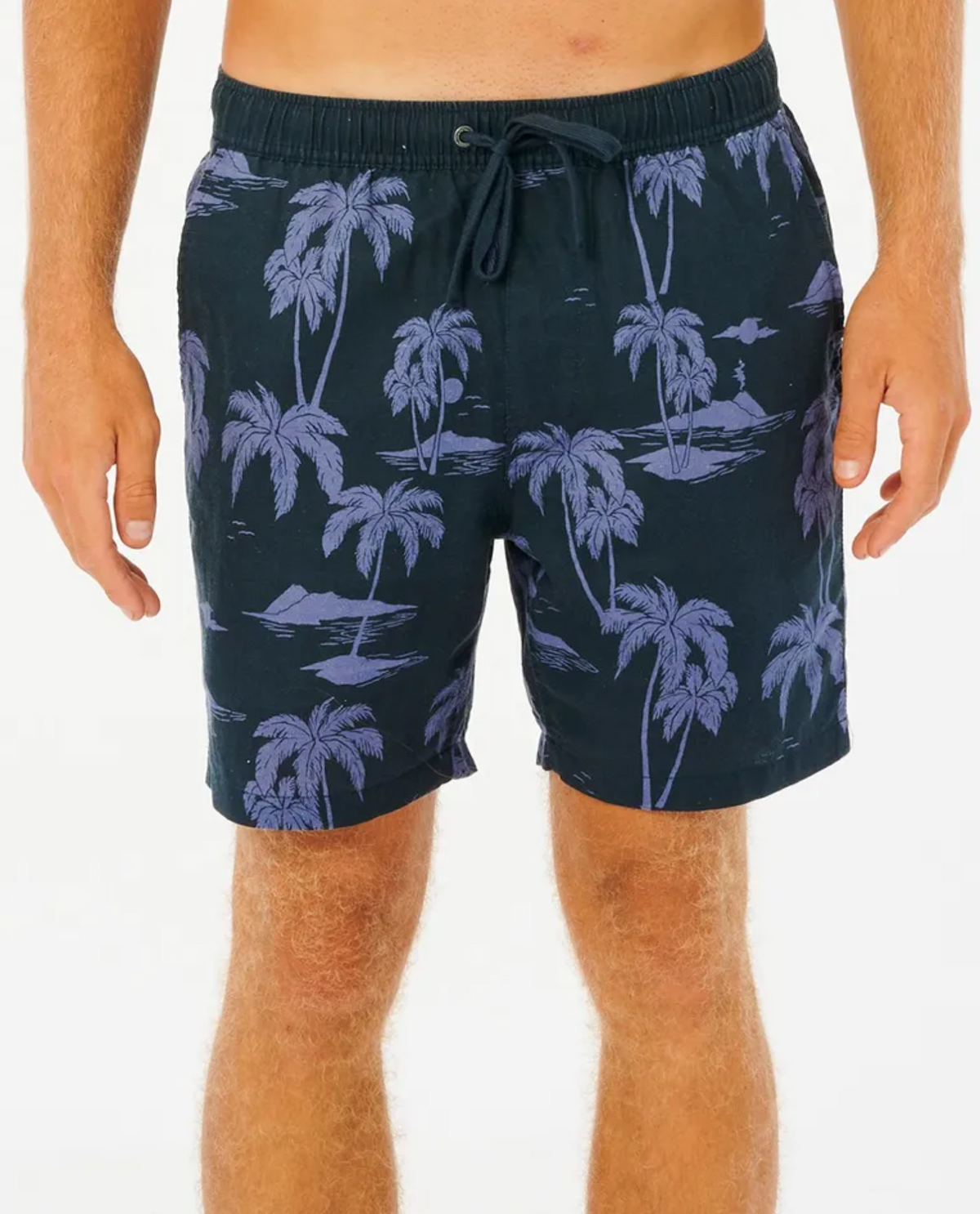 Wearing Rip Curl Mod Tropics Volley shorts, featuring a black design with a purple palm tree pattern and an elastic waist for comfort. The linen/cotton blend makes them ideal for sunny days. Their limbs are visible against a plain white backdrop.