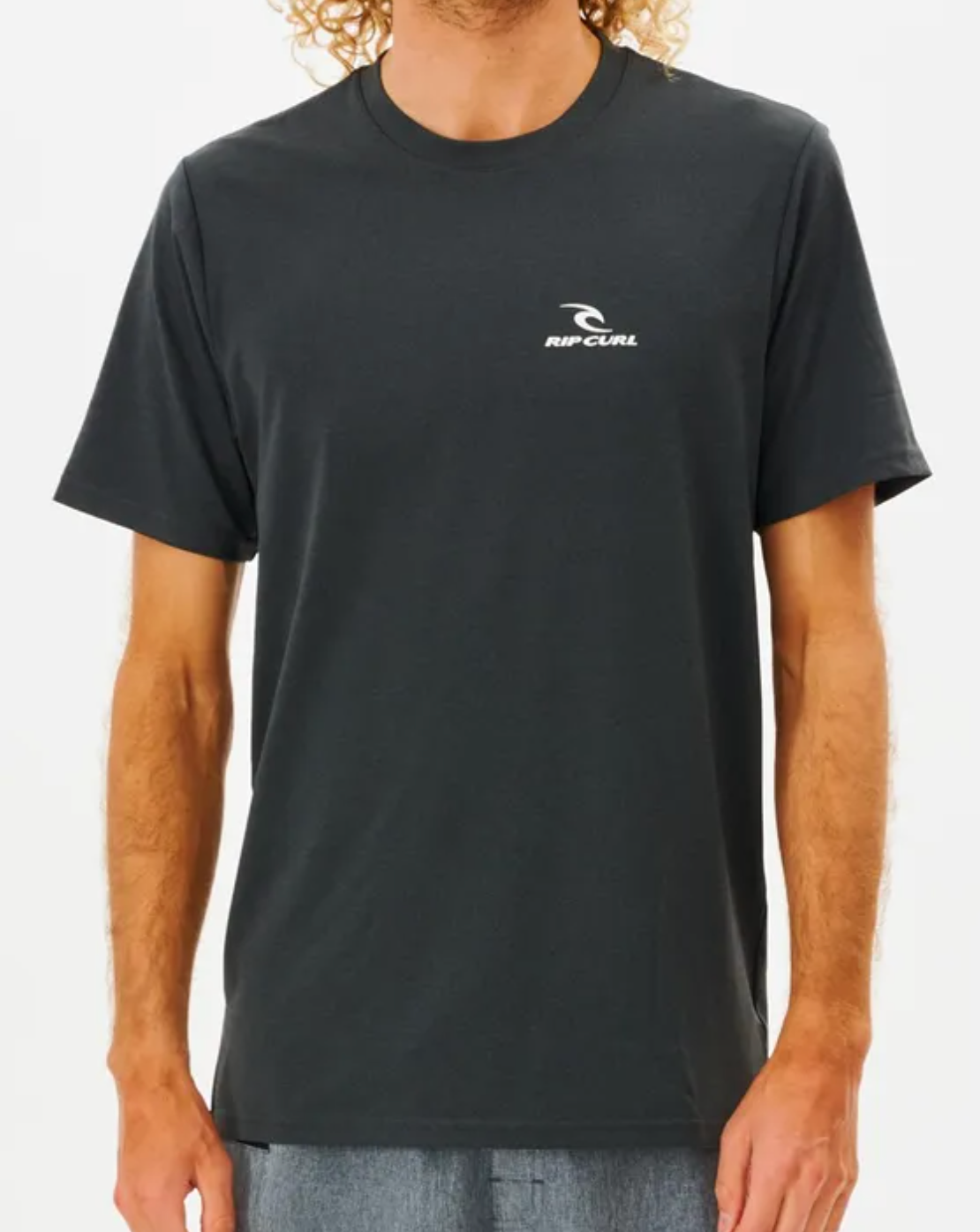 A person wears a black Rip Curl Search Series Tee with gray shorts, featuring a small white logo on the left chest. Its UPF 50+ protection is ideal for sunny days, set against a plain white background.