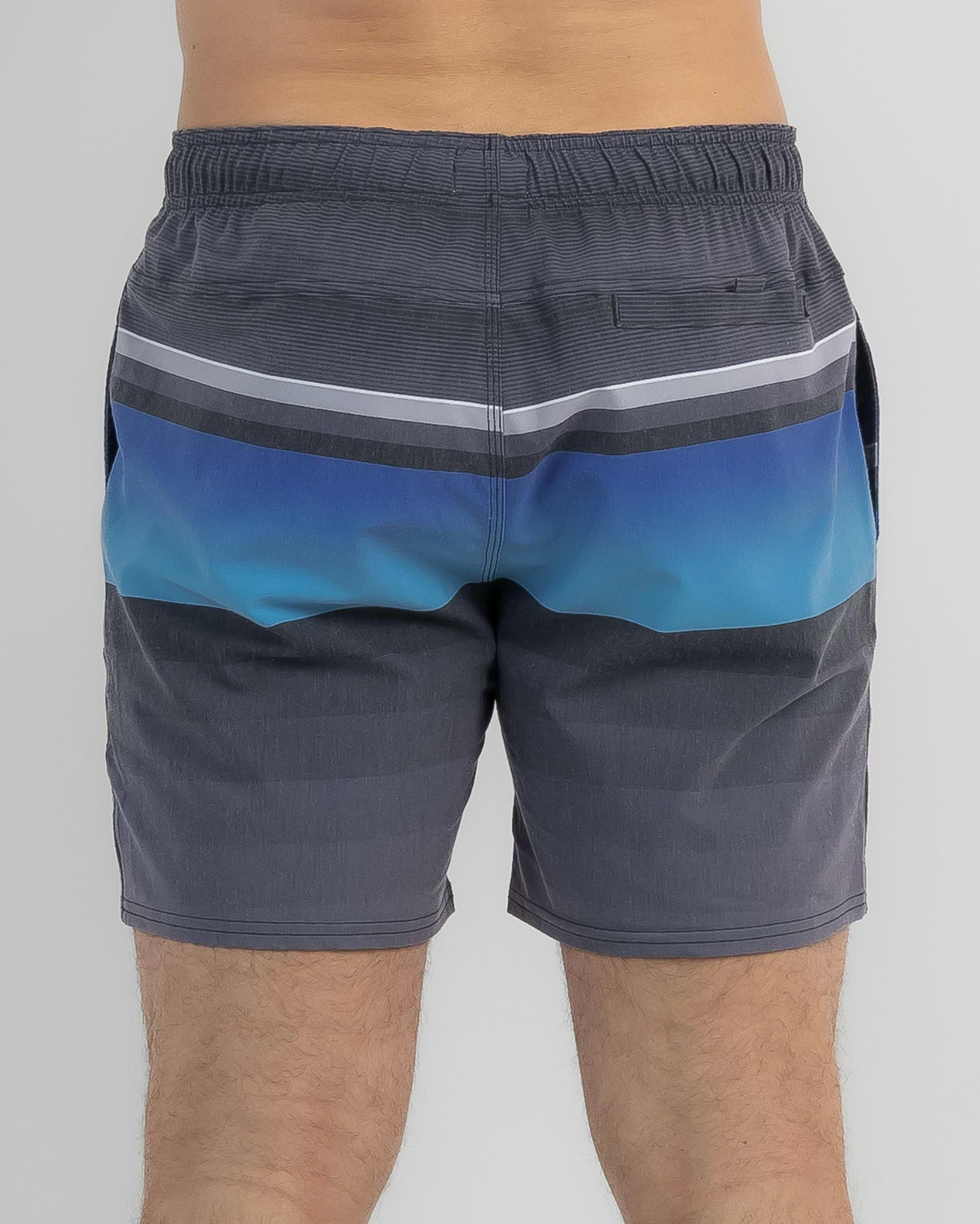 A person wears Rip Curl Party Pack Volley Shorts featuring a blue and gray gradient and elastic waistband, standing against a plain light background with only their torso and legs visible.