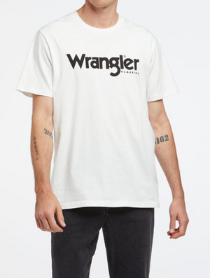 A person sports a Wrangler Classic Logo Tee, with black lettering, 100% cotton. Tattooed forearms complement the look, paired with sleek black jeans against a plain white background.