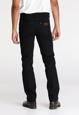 Dressed in Wrangler Classics Straight Jean, a person stands with their back to the camera. They wear a white shirt and brown shoes against a plain white backdrop.