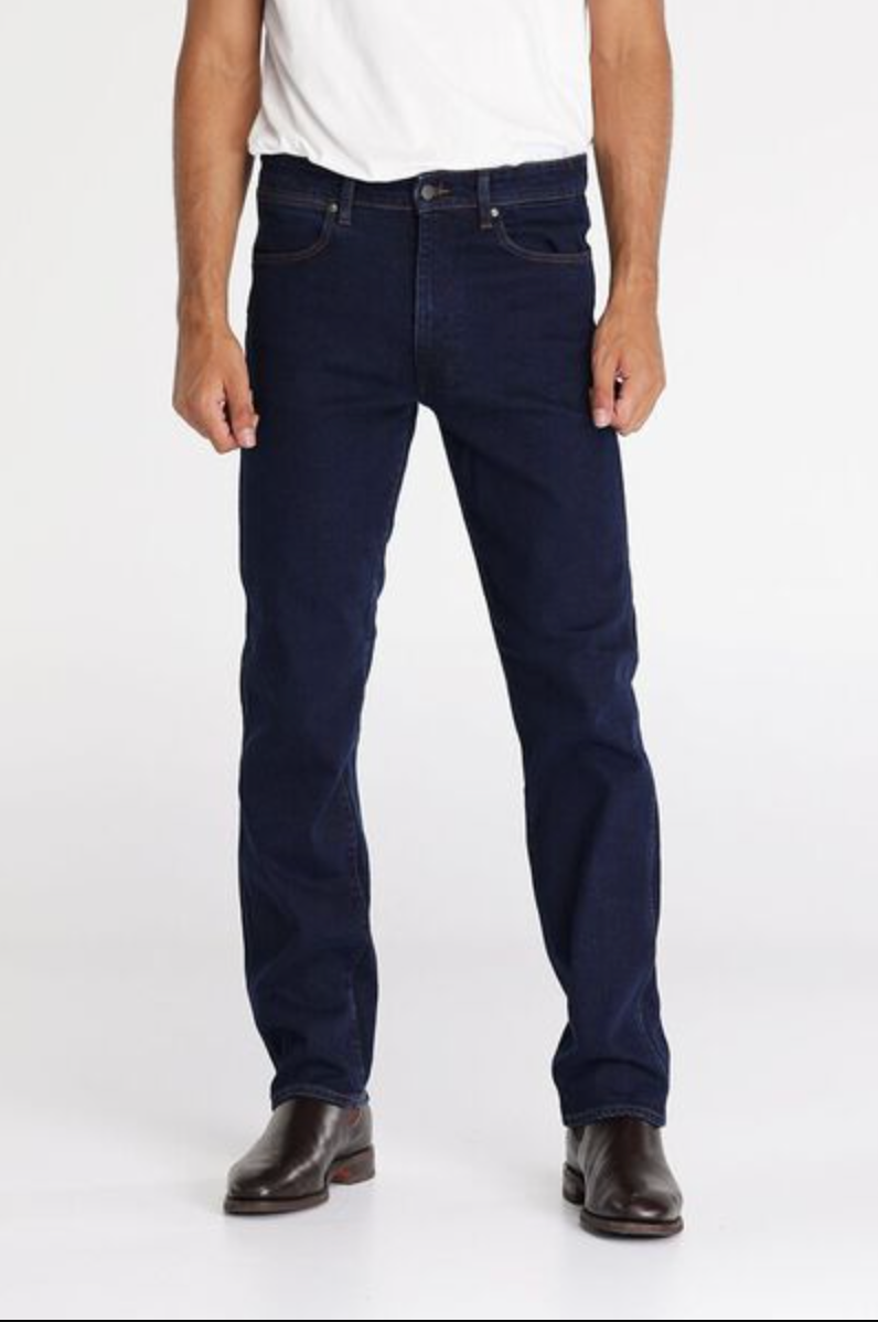 A person wears a white t-shirt tucked into dark blue Wrangler Classics Straight Jeans with brown leather belt loops and brown boots. The person is standing against a plain white background.