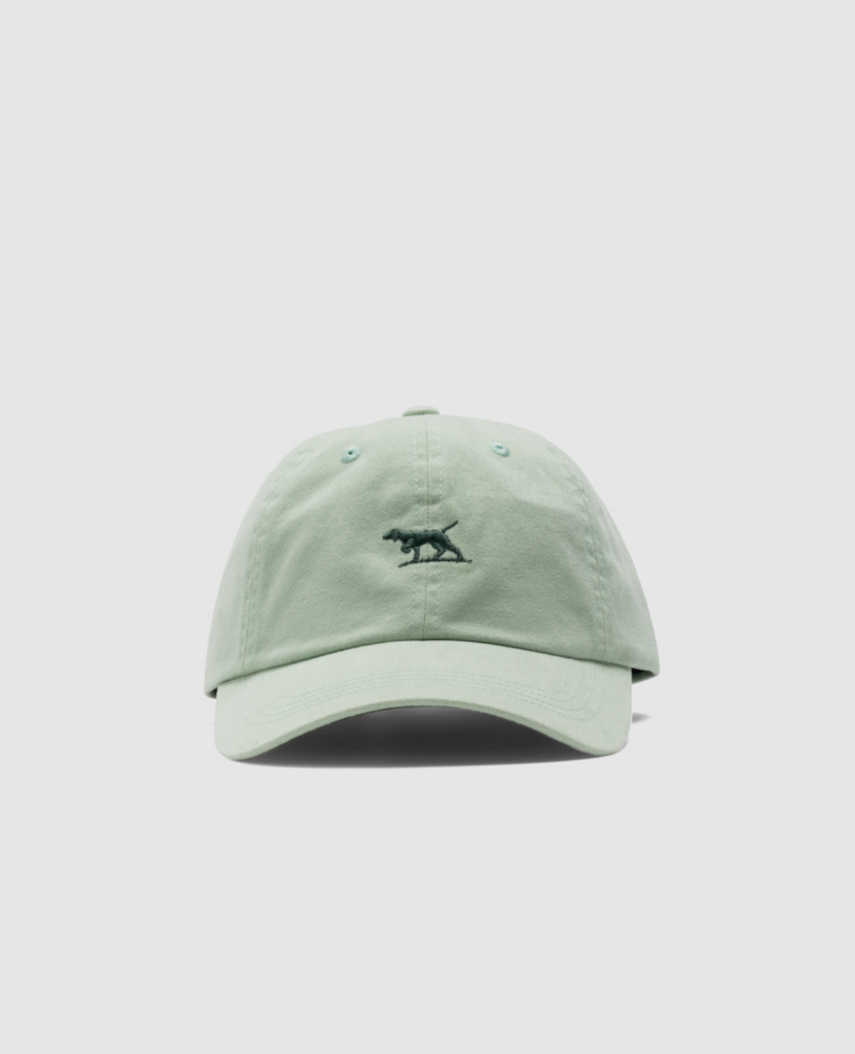 The Rodd & Gunn Gunn Cap is light green, made from 100% heavy-duty cotton twill. It features a small black embroidered dinosaur on the front, a curved brim, an adjustable strap, and is set against a plain white background.