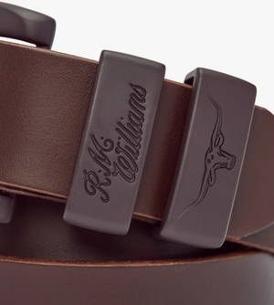 Close-up of the RM Williams Drover 1 1/2 Belt in brown, showcasing detailed accents with the R.M. Williams logo embossed on one section and a debossed Longhorn steer symbol on another. Crafted from vegetable-tanned leather, this belt features a rich, dark finish that highlights the texture and quality of the leather.