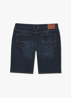 Back view of RM Williams Nicholson Short in dark blue stretch denim with a low-rise waistband, featuring Classic 5 pocket styling and visible stitching. The shorts have belt loops and a brown leather patch on the right side of the waistband. The fabric appears slightly worn or distressed.