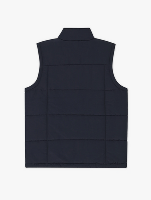 The RM Williams Patterson Creek Vest, crafted from Taslan nylon in navy blue, is shown from the back. It features horizontal stitching and a raised collar, and has no visible zippers or pockets to maintain a sleek and minimalist design. Additionally, it is water and wind resistant.