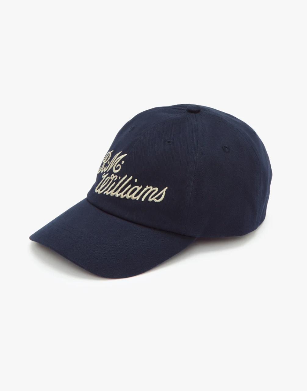 The RM Williams Script Cap is a dark blue hat featuring white embroidered cursive text that reads "R.M. Williams" on the front. It has a curved brim, six panels with ventilation eyelets, and comes against a plain white background.