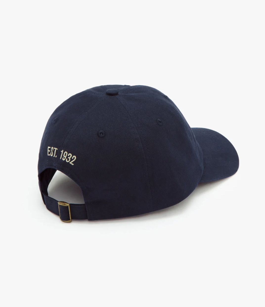 The RM Williams Script Cap in navy blue features white embroidered "EST. 1932" text on the back. This baseball cap includes a fabric strap with a brass-colored buckle for adjusting the size. The image displays the rear and a portion of the side of the cap against a plain white background.