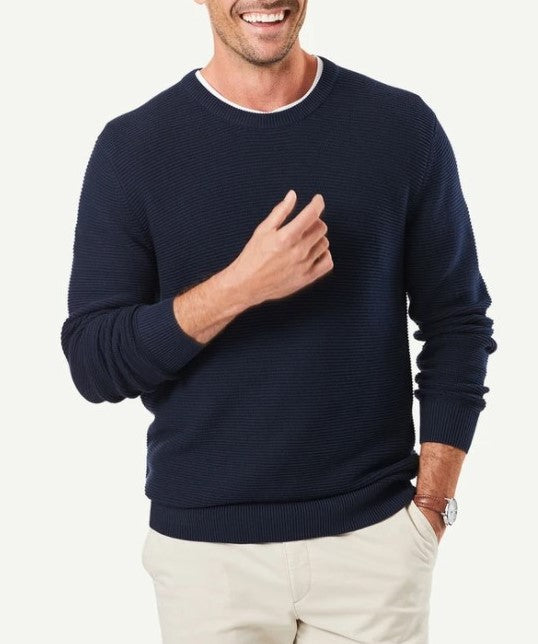 A person wearing a Gazman Textured Cotton Crew in navy blue, paired with a white collared shirt underneath, standing against a plain background. The person is smiling, has a light skin tone, and is casually posing with one hand on the side and the other hand slightly raised.