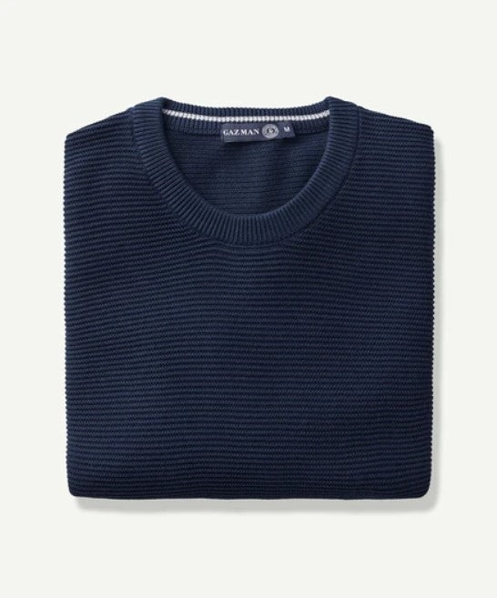 A neatly folded Gazman Textured Cotton Crew in navy blue, crafted from comfortable combed cotton, is shown against a plain background. The ribbed texture adds a touch of elegance, and a small tag at the neckline reads "GAZ MAN".