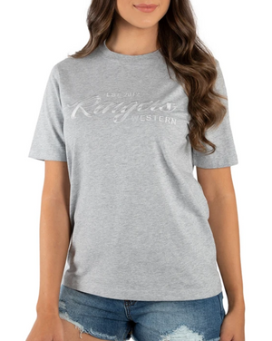 A woman wears a gray Ringers Western Womens Columbia Emboss Logo T-Shirt made of 100% cotton, displaying "EST. 2012." Her long, wavy brown hair flows over denim shorts against a plain white backdrop.