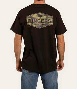 A person sports the Ringers Western Servo Loose Fit T-Shirt, featuring a camo-patterned hexagon logo reading "RINGERS WESTERN" on the back. Paired with blue jeans, it exemplifies casual style against a plain background.