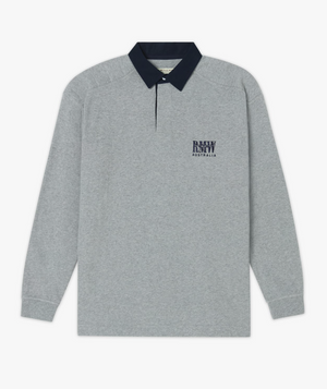 The RM Williams Classic RMW Rugby is a long-sleeved, grey polo shirt with a black collar made from heavy cotton jersey. It has a subtle and clean design featuring the RMW Longhorn logo and the text "Australia" printed in black on the left chest area, giving it a timeless rugby style.