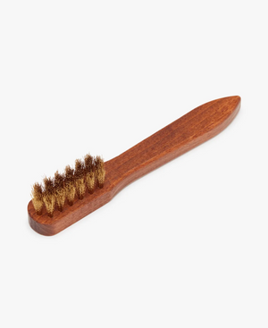 The RM Williams Suede Brass Bristle Brush features a wooden handle with dense, brown brass bristles arranged in a single row. The smooth, tapered handle offers a comfortable grip and precise control, making it ideal for cleaning tasks such as maintaining your suede boots.