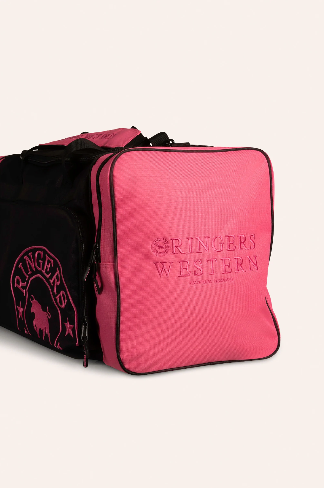 The Ringers Western Rider Sports Bag is a large, stylish sports bag with a pink square end panel featuring embroidered "Ringers Western" text. The rest of the bag is black with pink accents and a bull logo on the side. It includes multiple compartments and zippers, making it perfect for all your gear.