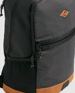 The Billabong Norwest Pack features a gray and black design, accented with a small brown patch on the corner. It includes dual zippers, a brown base, durable material texture, and ergonomic shoulder straps for comfort.