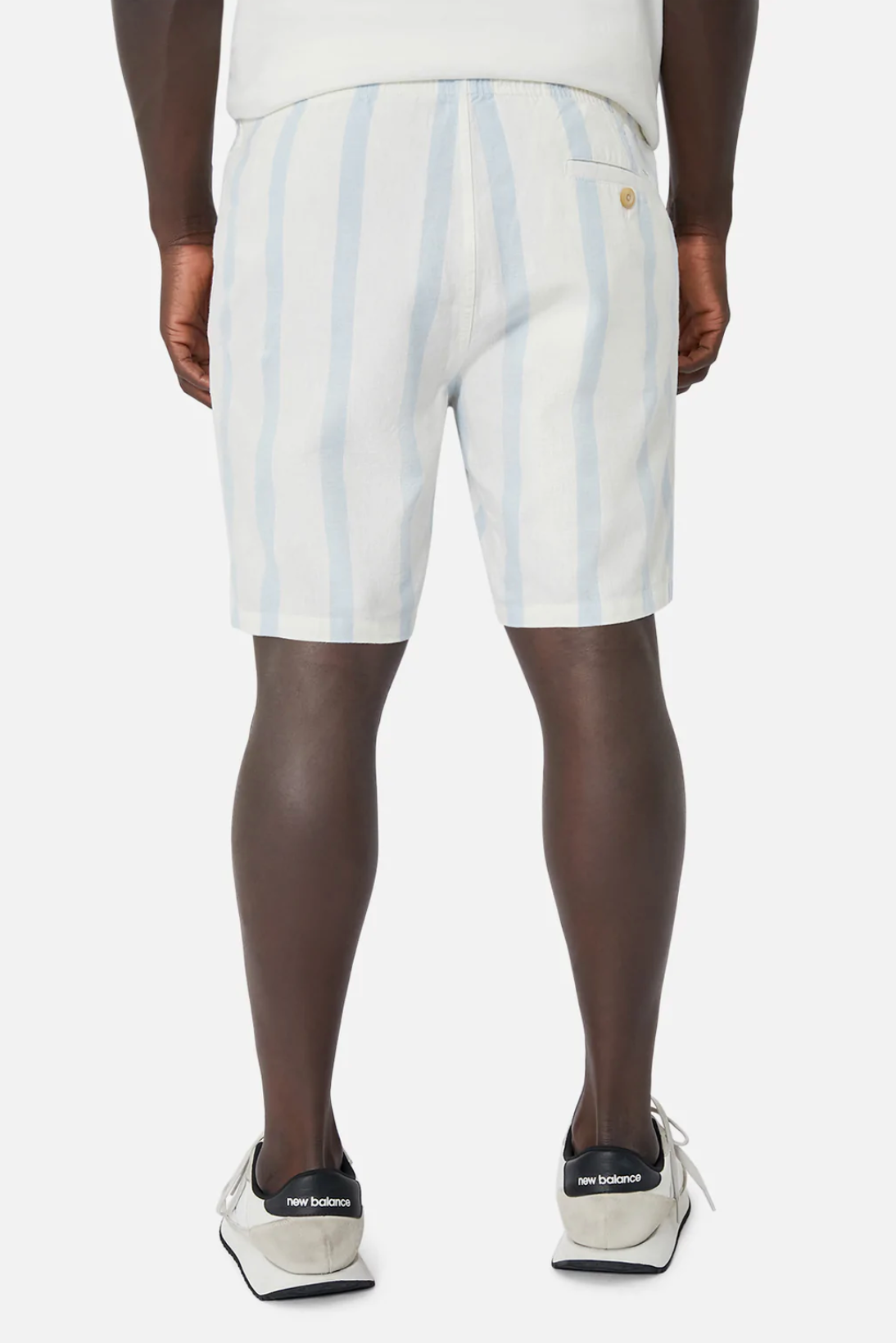The person is wearing Industrie The Mykonos Short, which features white and light blue stripes with an elastic waist, paired with white sneakers accented in black. The background is plain white, and the perspective shows the back view.