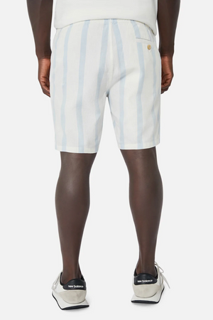 The person is wearing Industrie The Mykonos Short, which features white and light blue stripes with an elastic waist, paired with white sneakers accented in black. The background is plain white, and the perspective shows the back view.