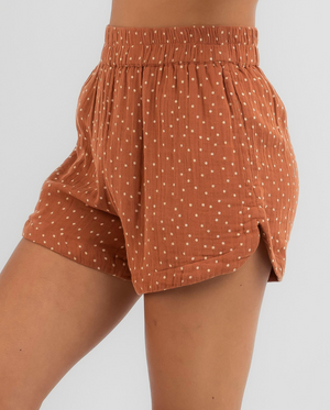 A person wearing high-waisted Rip Curl Premium Surfa Shorts in rust with white polka dots and an elastic waistband. These relaxed-fit cotton shorts include side slits for extra comfort.