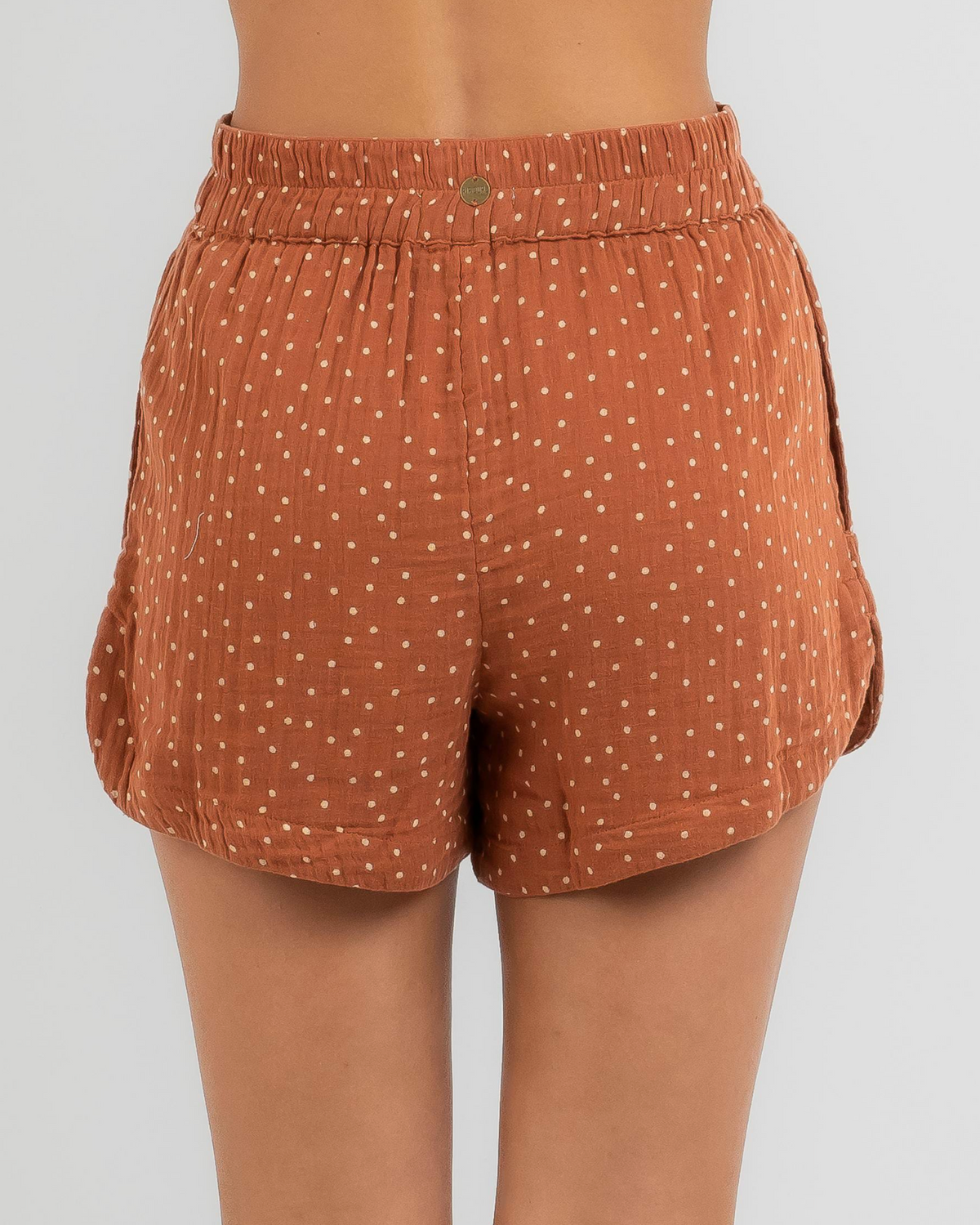 A person wearing Rip Curl Premium Surfa Short, high-waisted and loose-fitting, in rust with white polka dots, featuring an elastic waistband and a front button.