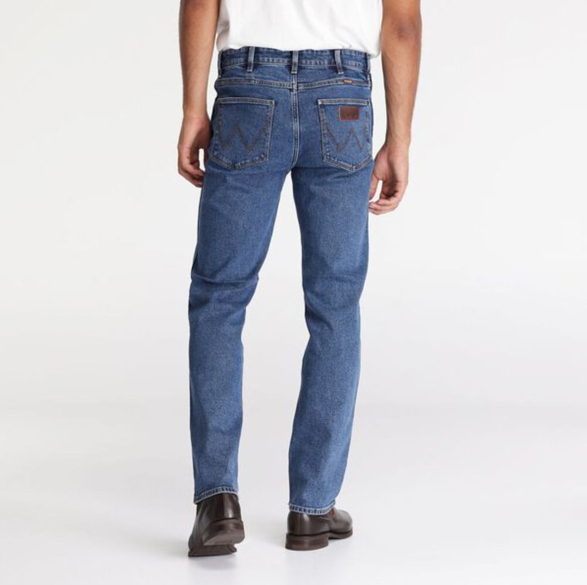 Rear view of someone in a white shirt, brown shoes, and mid-rise Wrangler Classics Straight Jean with unique stitching on the back pockets, all set against a plain white background.