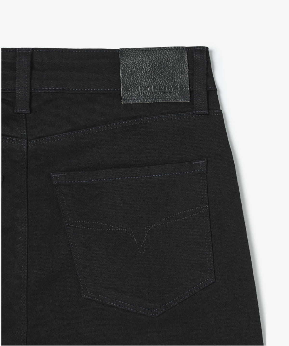 Close-up shot of the back pocket of a pair of RM Williams Albury Jean in black. The pocket features minimalist stitching, and there is a leather patch with text on the waistband above it. Made from stretch cotton, these high-rise skinny fit jeans also showcase subtle Longhorn embroidery for a touch of flair.