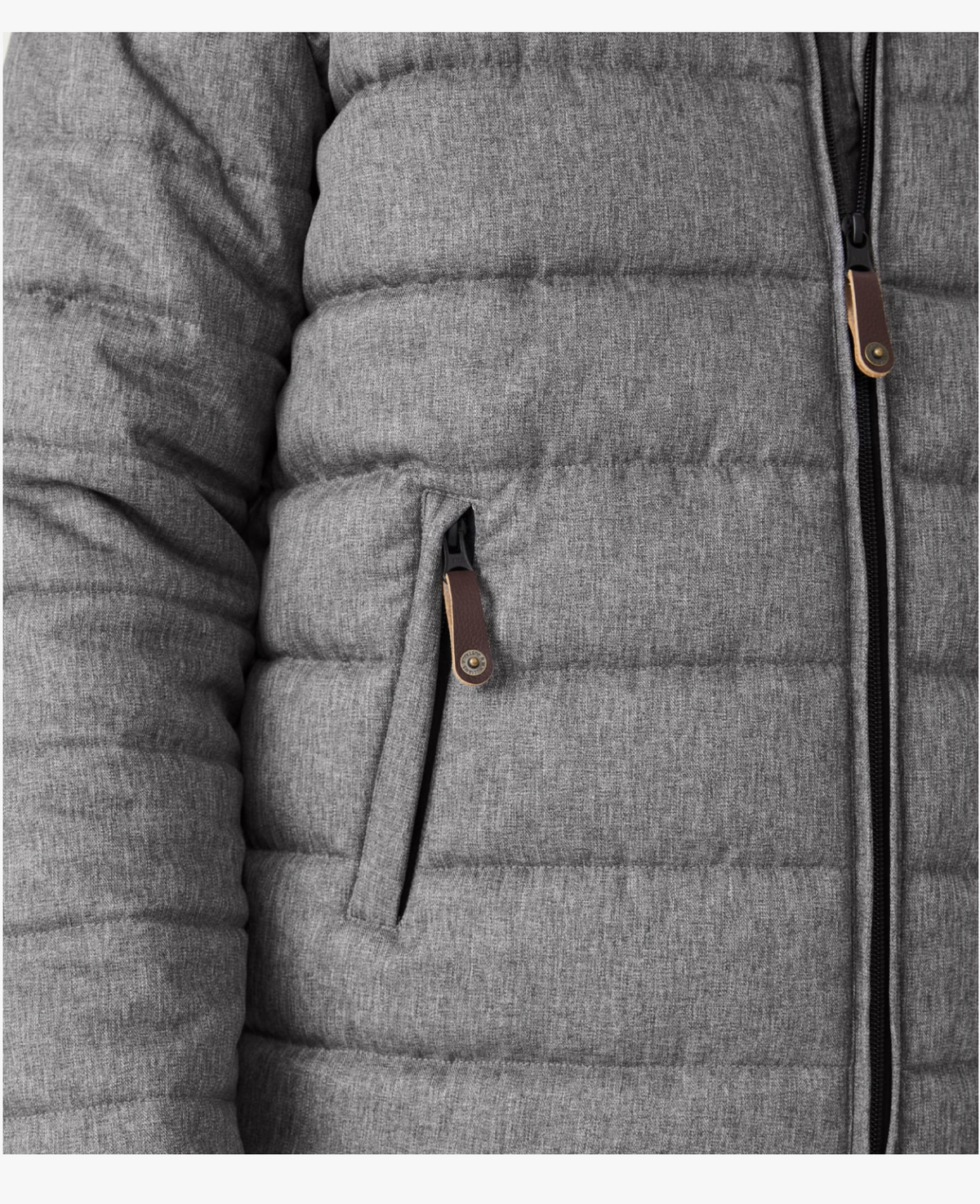 A close-up of the RM Williams Patterson Creek Jacket showcases its quilted gray design with horizontal stitching. It features a partially visible vertical main zipper, a zippered side pocket with a brown leather pull tab, and is crafted from soft, insulated, durable polyester twill.