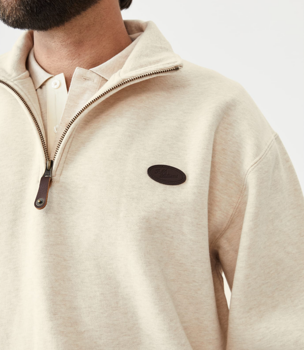 Close-up of a bearded man wearing the RM Williams Mulyungarie Fleece, a light beige quarter-zip pullover made from brushed cotton, with a leather zipper pull and an oval leather chest patch. He's sporting a white shirt underneath, embracing a vintage style.