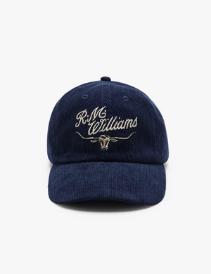 The RM Williams Corduroy Longhorn Cap, crafted in navy blue cotton corduroy, features elegant cursive "R.M. Williams" embroidery and a longhorn emblem beneath, all on a plain white background.