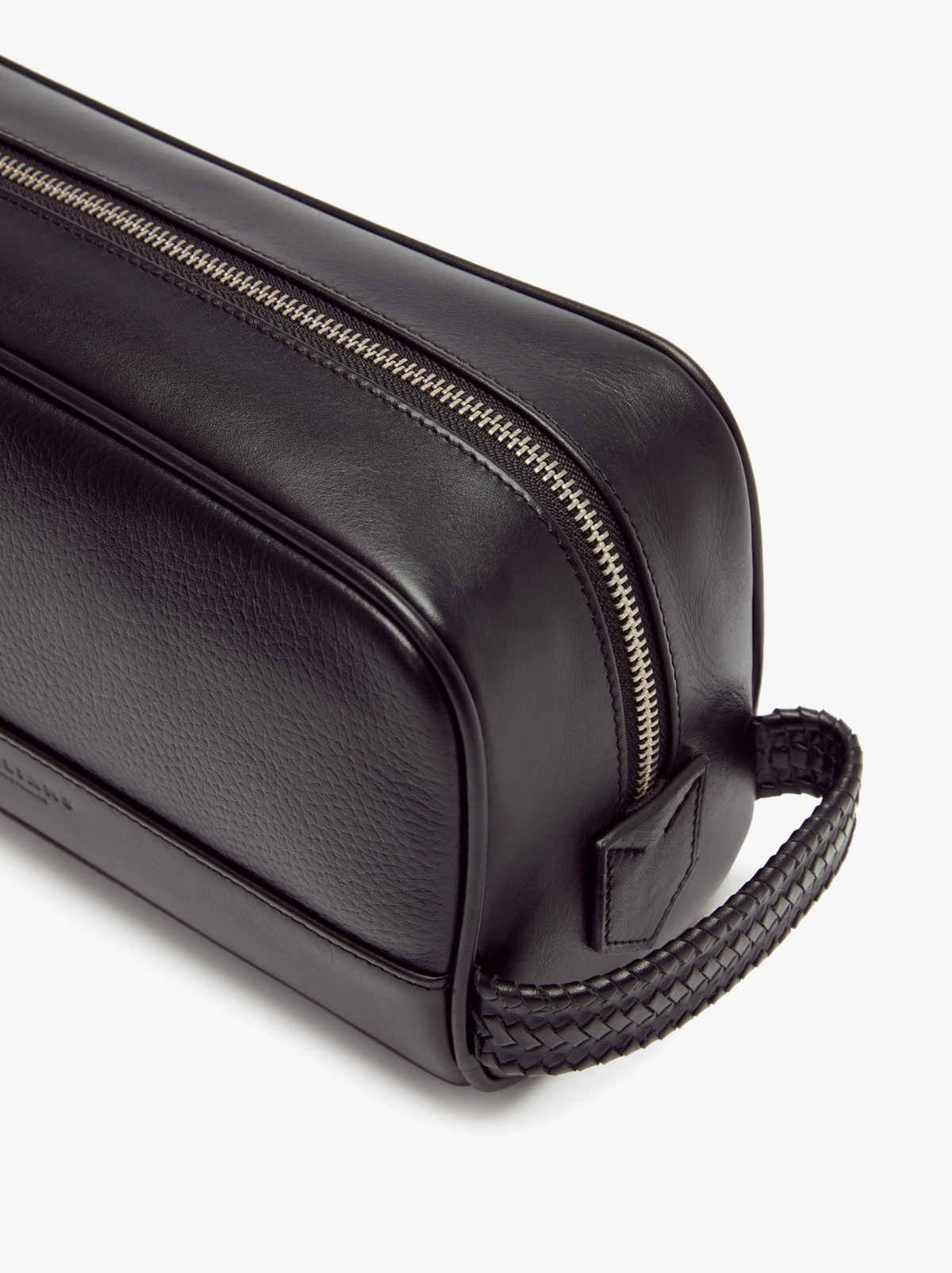 A close-up view of the RM Williams City Washbag showcases its black full grain leather construction with a silver zipper. The bag includes a textured handle on one end, offering a minimalist and sleek design with clean lines and a smooth finish.