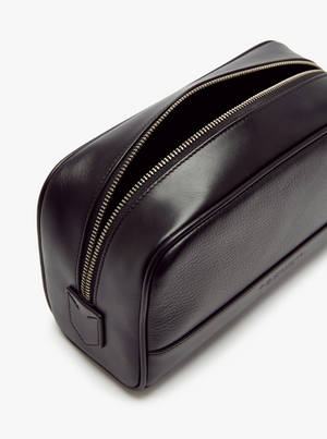 The RM Williams City Washbag is a sleek, rectangular-shaped toiletry bag made from black full-grain leather. It features a single zipper along the top, partially open to showcase its spacious interior. The washbag has a smooth, slightly glossy finish with a small embossed logo on one end.