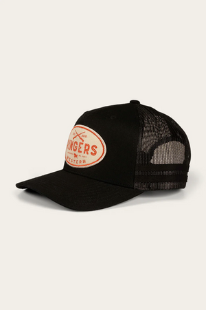 The Ringers Western Deacon Trucker Cap is black with a mesh back and curved brim, made from durable cotton twill. It features a white oval patch with red text and small crossed graphics on the front, capturing the iconic Ringers Western style.