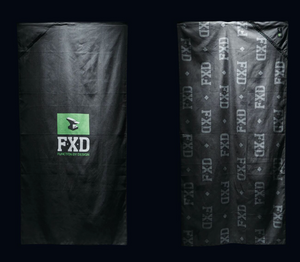 Two black FXD WAT-1 X Slowtide Work Towels are shown against a dark background. The left towel has a green "FXD" logo with "FUNCTION BY DESIGN," made from recycled polyester, while the right towel displays a gray fast-drying repeated "FXD" pattern.