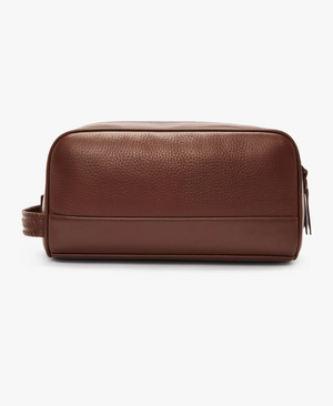 The RM Williams City Washbag, made from full grain leather with a textured surface and a zippered closure, comes in a sleek brown color. This dopp kit, highlighted against a plain white background, is designed with a sturdy handle on one side for easy carrying.