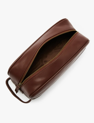 The RM Williams City Washbag, crafted from full grain brown leather, features a gold zipper partially open to reveal a patterned interior lining. With a handle on one side for easy carrying, this stylish toiletry bag is perfect for urban adventures.